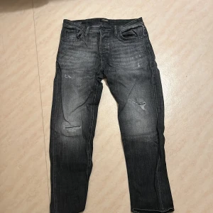 Grå jeans med slitningar - Säljer ett par grå jeans med coola slitningar och en tapered passform. Perfekta för en avslappnad stil. 