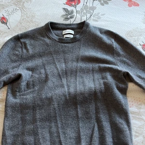 Grå merinoulltröja från These Glory Days - Säljer en stilren grå tröja från These Glory Days i mjuk merinoull. Perfekt för kyliga dagar med sin klassiska design och bekväma passform. Tröjan har rund hals och långa ärmar.