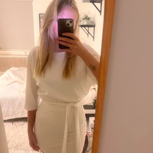 Vit klänning med knytband - Helt ny med prislapp och i orginalförpackning, vit klänning med trekvartsärm och knytband i midjan. Perfekt som studentklänning men även till annat. Kostar 500kr på hemsidan och aldrig använd