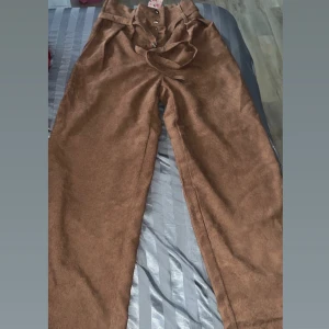 Bruna manchesterbyxor med knytband -  bruna manchesterbyxor med hög midja och knytband. Byxorna har en dragkedja och knappar framtill för enkel stängning. Perfekta för en stilren look.