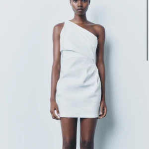 Vit oneshoulder klänning från Zara - Snygg vit oneshoulder klänning från Zara. Helt ny! Prefekt till studenten. Perfekt för en stilren look med sin korta längd och eleganta design. Klänningen har en asymmetrisk axel och en figurnära passform.