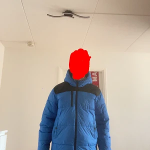 Blå dunjacka från Boss - Säljer en blå dunjacka från Boss med svarta detaljer och en hög krage. Jackan har en dragkedja framtill och är perfekt för kalla dagar. Den har en pufferdesign som ger extra värme och stil. Skriv gärna vid fler frågor. Den är lite sönder på sidan. Priset kan diskuteras vid snabb affär!!! 