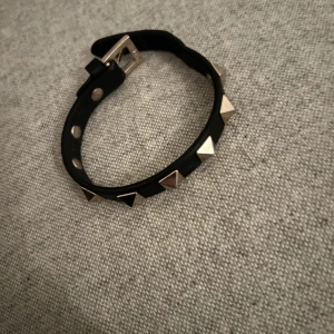 Svart armband med nitar från Valentino - Snyggt svart armband från Valentino med guldnittar. Armbandet har ett justerbart spänne och kommer i originalförpackning med tillhörande påse. Väldigt bra skick och äkta såklart! 