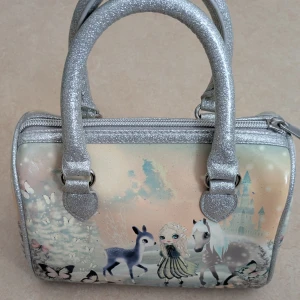 Söt handväska med sagomotiv - Charmig handväska med ett magiskt sagomotiv av en flicka, hjort och häst. Väskan har glittriga silverhandtag och dragkedja. Perfekt för att lägga till en touch av fantasi till din stil. Köpt på HM 