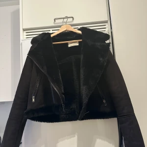 Svart jacka med päls från Stradivarius - Jackan har dragkedjor på sidorna och en croppad design som ger en modern look. Liten i storlek!