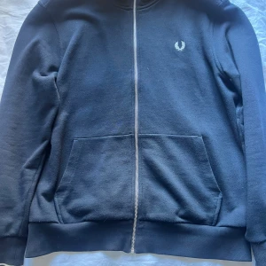 Mörkblå zip-hoodie från Fred Perry  - Mörkblå hoodie från Fred Perry i storlek XL med dragkedja hela vägen, två stora fickor fram och klassisk logga på bröstet. Nypris 1500