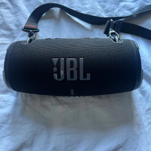 JBL Xtreme 3 - JBL Xtreme 3 är en kraftfull, bärbar Bluetooth-högtalare med robust design och axelrem för enkel transport. Den har USB-C och AUX-ingång, tydliga kontrollknappar och är i gott skick med mindre kosmetiska märken på loggan. Nypris 3300kr