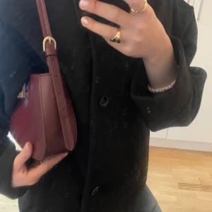 Vinröd väska med guld detaljer  - Vinröd axelväska med justerbart band och snygga guld detaljer, Perfekt till hösten, har ett litet fack med dragkedja inuti väskan 