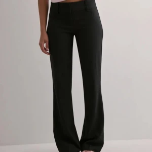 Svarta lågmidjade bootcut kostymbyxor - Nya snygga svarta kostymbyxor med klassisk rak passform och normal midja. Byxorna har diskreta fickor och stängs med dragkedja och knapp. Perfekta för en clean och stilren look. Säljer eftersom jag beställde men testade min kompis byxor innan mina kom. Så har ett par helt nya i original förpackningen