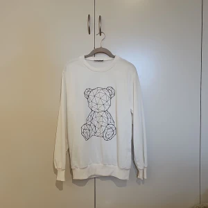 Vit sweatshirt med björntryck från Eiger - Vit sweatshirt från Eiger Sportswear med ett coolt geometriskt björntryck på framsidan. Tröjan har rund hals, ribbade muddar och är långärmad. Perfekt för dig som gillar stilrena och unika prints.
