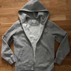 Jack & Jones grå ziptröja - Stilren och bekväm ziptröja i mjukt material med huva och hel dragkedja. Perfekt för vardag och fritid.