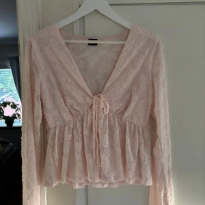 Ljusrosa spetsblus med knyt - Supersöt ljusrosa blus från Gina tricot  i transparent spets med v-ringning och knyt framtill. Blusen har långa ärmar. Perfekt att styla med jeans eller kjol för en söt look.
