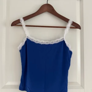 Blå linnetopp med vit spets - Supersöt blå linnetopp med tunna axelband och vit spets längs kanterna och banden. 💙