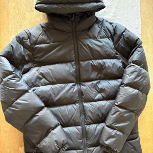 Svart vinterjacka  från Neomondo - Säljer en svart vinterjacka från Neomondo i storlek S. Jackan har en hög krage, huva och dragkedja framtill. Den är vadderad och har elastiska muddar vid ärmsluten. Perfekt för kalla dagar när du vill hålla dig varm och bekväm.