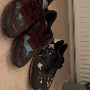 Valentino Rockrunner sneakers camo - Säljer två par Valentino Rockrunner sneakers. Ena paret har camouflagemönster i blått, vinrött och grönt med vinröda snören och detaljer i skinn och mocka. Det andra paret är svart och beige med stjärndetaljer bak och nitar på hälen. Båda har platt sula och coola detaljer. 1800 styck ellr bättre pris vid köp av båda. Skriv för frågor!