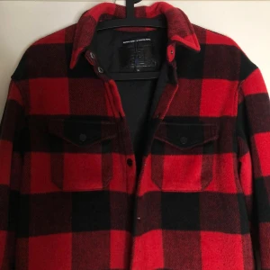 Röd och svart rutig overshirt - Riktigt snygg overshirt i röd och svart rutig design från Beautiful Denim x Beautiful People. Skjortan har klassisk krage, två bröstfickor med lock och knappar framtill. Perfekt lager-på-lager-plagg med lång ärm och mjukt material.