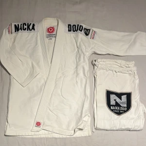 Vit jiu-jitsu gi från Chokem Nacka Dojo - Säljer en vit jiu-jitsu gi från Chokem med stora Nacka Dojo-patchar på både jacka och byxor. Jackan har broderade loggor på axlarna och ryggen, byxorna har dragsko och matchande patch. Den är utrustad med alla nödvändiga patches för tävling för Nacka Dojo. Säljes eftersom jag har växt ur den. 