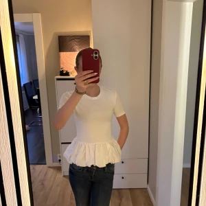 Vit peplum topp från Gina Tricot - Supersöt vit peplum topp från Gina Tricot i storlek S. T-shirttopp med rund hals, korta ärmar och volang nertill som ger en snygg siluett. Perfekt att styla med jeans eller kjol för en trendig look. Helt ny men fel storlek för mig.