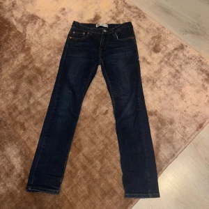 Levi's 512 Slim Taper jeans mörkblå - Mörkblå Levi's 512 Slim Taper jeans med klassiska fem fickor, snygga kontrastsömmar och ikonisk läderpatch bak. Jeansen har smal passform med avsmalnande ben och är tillverkade i slitstarkt denimtyg. Perfekta för dig som gillar en clean och modern look.