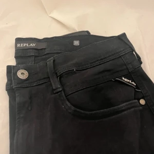 Svarta Replay jeans, modell Anbass - Snygga svarta jeans från Replay, modell Anbass. Klassisk femficksdesign med silverfärgade knappar och detaljer. Jeansen har en smal passform och är tillverkade i stretchigt bomullsmaterial för extra komfort.