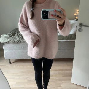 Ljusrosa fluffig stickad tröja - Supermysig ljusrosa stickad tröja med oversized passform och långa ärmar. Tröjan är fluffig och har en enkel rund halsringning. Perfekt för dig som gillar en chill och avslappnad stil under kyliga dagar.