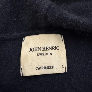 Mörkblå cashmere hoodie John Henric - Mjuk och lyxig mörkblå hoodie från John Henric i 100% cashmere. Klassisk modell med huva och snörning, samt känguruficka framtill. Perfekt för dig som vill ha en stilren och bekväm tröja med premiumkänsla. Avgör skick själv så inge fel kommer upp