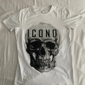 Vit t-shirt med döskalle från Icono - Vit t-shirt från Icono i regular fit med ett stort döskalletryck framtill dekorerat med små glittrande detaljer. 