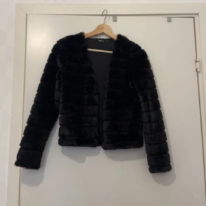 Svart pälsjacka från Gina Tricot - Säljer en svart pälsjacka från Gina Tricot i storlek XXS. Jackan är kortare i modellen, har lång ärm och är tillverkad i mjukt fuskpälsmaterial med horisontella sömmar för en cool look. Perfekt för dig som vill sticka ut med en trendig och mysig jacka.