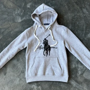 Grå hoodie från Polo Ralph Lauren - Exklusiv grå Polo Ralph Lauren-hoodie med svart polospelare. Svår att få tag på och perfekt för en skön, stilren look.