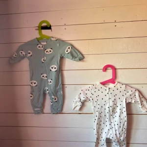 Två mjuka sparkbyxor med mönster - Säljer två gulliga sparkbyxor för baby, en vit med svarta prickar och en ljusblå med söta pandamotiv. Båda har långa ärmar och ben samt dragkedja framtill för enkel påklädning. Perfekta för mysiga dagar hemma.
