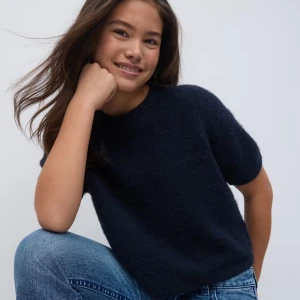 Mörkblå stickad tröja med kort ärm - Snygg mörkblå stickad tröja med korta ärmar och rund hals. Modellen är lite loose och har en mjuk, fluffig känsla som gör den extra skön. Perfekt att styla med jeans eller kjol för en chill look.