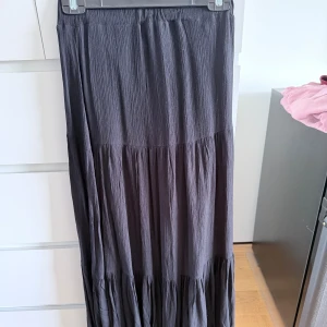 Svart långkjol från & Other Stories - Säljer en svart långkjol från & Other Stories i storlek XXS. Kjolen har en volangig design med flera lager och resår i midjan. Materialet är lätt och har en krinklad struktur som ger en avslappnad känsla. Perfekt för dig som gillar en flowy och stilren look.