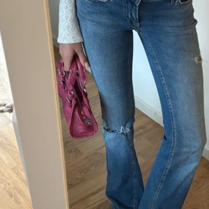 Mörkrosa handväska med detaljer - Säljer en snygg mörkrosa handväska i skinnimitation med silvriga metalldetaljer och dubbla handtag med flätad look. Väskan har spännen framtill och dragkedja upptill. Perfekt storlek för det viktigaste och ger en cool touch till din outfit.