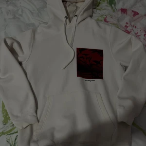 Vit hoodie från Jack & Jones - Vit hoodie från Jack & Jones med tryck i rött och svart framtill och text på ryggen. Tröjan har huva med snörning och en stor magficka. Skön och avslappnad passform, perfekt för chill dagar.