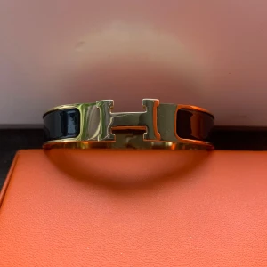 Svart H armband - Exklusivt H armband i svart och guld. Låda och påse tillkommer. Perfekt för dig som vill ha en exklusiv och stilfull accessoar. Pris kan diskuteras.