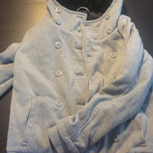 Ljusgrå dubbelknäppt jacka FB Sister -  Snygg detalj med texten 'LIMITED CHALLENGE' längs ena sidan. Perfekt för kyliga dagar.