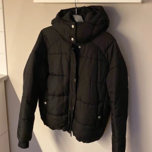 Svart pufferjacka från 157, XS - Säljer en svart pufferjacka från 157 i storlek XS. Jackan har huva, knappar och dragkedja framtill samt två fickor med tryckknappar.