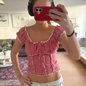 Rutig röd blus från Urban Outfitters - Supersöt röd- och vitrutig blus från Kimchi Blue med volangdetaljer, knyt framtill och spetskant vid halsringningen. Croppad modell med korta puffärmar och smockad midja. Perfekt för dig som gillar romantisk och lekfull stil. Pris kan diskuteras 