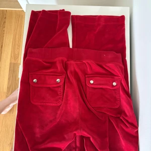 Röda mjukisbyxor med fickor - Snygga röda mjukisbyxor i mjukt material med två bakfickor med lock och silverfärgade knappar. Byxorna har resår i midjan och raka ben. Perfekta för en chill och avslappnad stil.