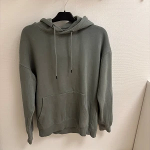 Grå hoodie från Jack & Jones - Säljer en stilren grå hoodie från Jack & Jones med klassisk känguruficka och huva med snörning. Tröjan har en relaxed passform och är tillverkad i mjuk bomull, perfekt för chill dagar eller när du vill ha en enkel look.