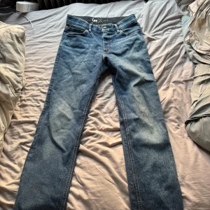 Blå raka jeans från Lee - Säljer ett par klassiska blå jeans från Lee med raka ben och femficksmodell. Jeansen har normal passform och är tillverkade i slitstarkt denimtyg. Perfekta för dig som gillar en tidlös och enkel stil.
