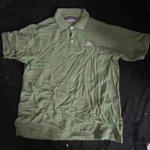 Grön pikétröja från Kappa - Snygg grön pikétröja från Kappa i storlek Large. Klassisk krage med två knappar och Kappa-logga broderad på bröstet. Tillverkad i mjuk bomull, perfekt för en avslappnad och sportig look.