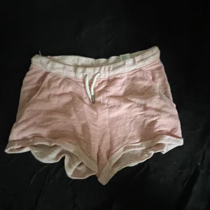 Rosa frottéshorts med snörning - Mjuka och sköna rosa shorts i frotté med vit dragsko i midjan. De har en avslappnad passform och elastisk midja, perfekta för lata dagar eller när du vill chilla hemma. Shortsen har en sportig vibe och är riktigt bekväma.