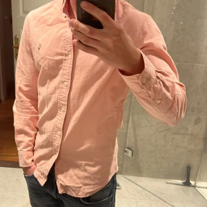Polo Ralph Lauren Skjorta - Säljer en snygg rosa skjorta från Polo Ralph Lauren i slim fit-modell. Skjortan är i stretchig bomull, har klassisk krage med knappar och det ikoniska broderade logot på bröstet. Perfekt för dig som gillar stilrena och fräscha plagg.