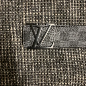 Louis Vuitton Damier Graphite bälte - Snyggt Louis Vuitton bälte i Damier Graphite-mönster med klassiskt LV-spänne i mörk metall. Bältet är gjort i svart skinn och har diskret rutigt mönster längs hela bandet. Perfekt accessoar för att lyfta din outfit med en lyxig touch.