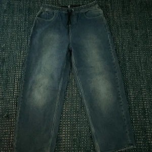 Blå loose jeans från Volcom - Säljer ett par blå jeans från Volcom med elastisk midja och snörning. Byxorna har raka ben, två fickor fram och två bakfickor. Jeansen har en avslappnad loose passform och är tillverkade i klassiskt denimtyg. Volcom-logga syns på bakfickan och vid benslutet.