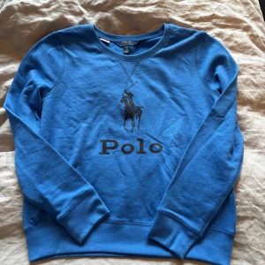 Blå sweatshirt från Polo Ralph Lauren - Blå sweatshirt från Polo Ralph Lauren med klassiskt tryck av polospelaren och Polo-loggan på bröstet. Tröjan är gjord i mjuk bomull. Perfekt för en chill och stilren look. Storlek 16 år motsvarar xs-s 