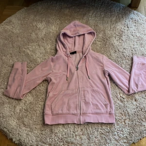 Rosa frotté hoodie med dragkedja - Mysig rosa hoodie i frotté med huva och snörning. Tröjan har dragkedja framtill, två fickor och långa ärmar. Perfekt för chill dagar eller när du vill ha en skön och mjuk look.