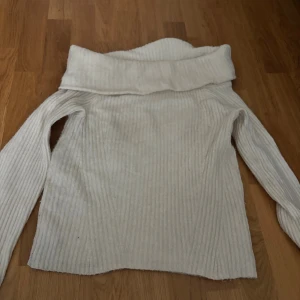 Vit ribbad polotröja i stickat material - Mysig vit polotröja med bred krage och ribbat stickat material. Tröjan har lång ärm och är perfekt för kyliga dagar. Enkel att matcha med jeans eller kjol för en clean och stilren look.