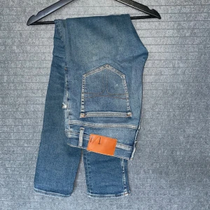 Blå jeans från Tiger of Sweden - Snygga blå jeans från Tiger of Sweden med klassisk femficksdesign och ljusa slitningar framtill. Jeansen har raka ben och normal passform, tillverkade i bomull med en skön känsla. Perfekta för dig som gillar stilrena och tidlösa jeans.